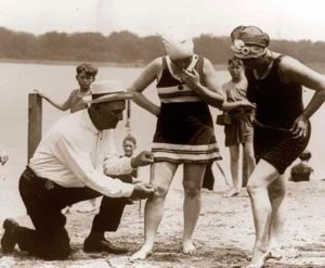 Patrulheiros na praia medindo o comprimento de trajes de banho das mulheres na década de 1920.